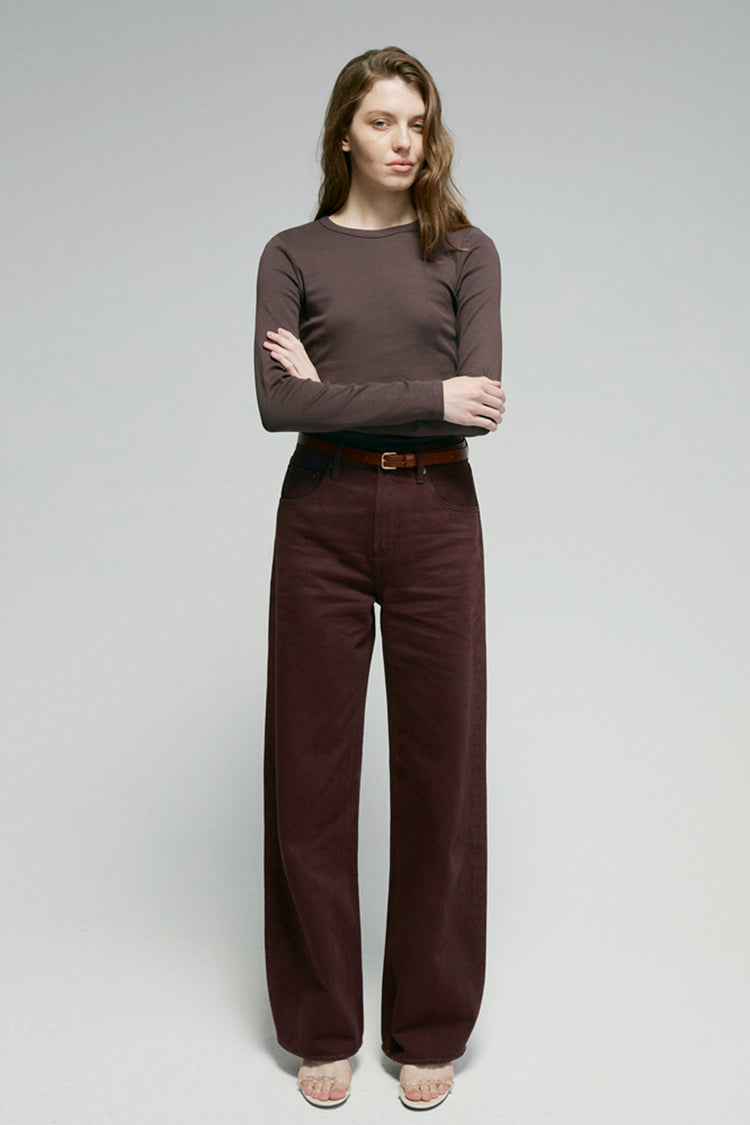 Woman wearing a brown long-sleeve top and dark brown pants on a gray background