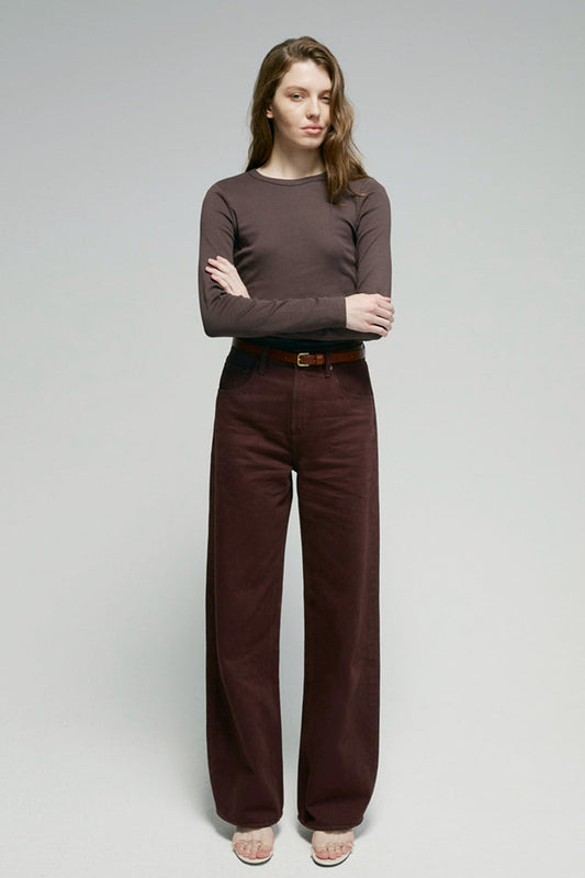 Woman wearing a brown long-sleeve top and dark brown pants on a gray background