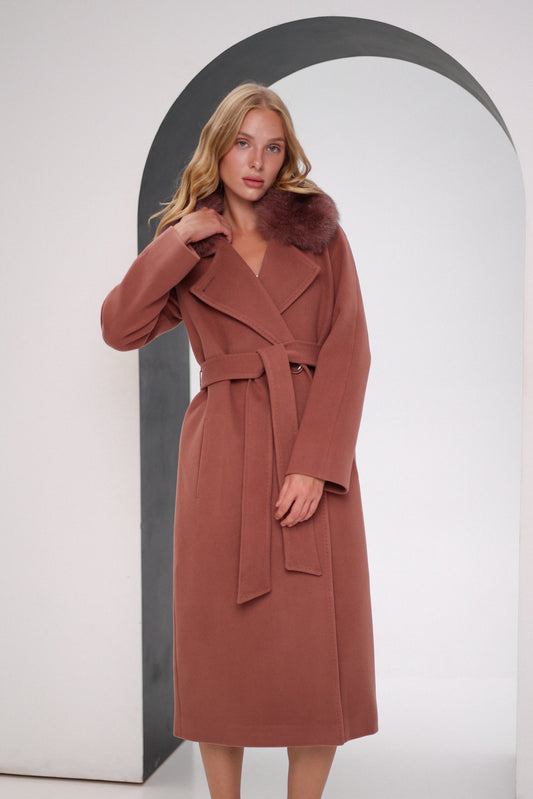 Woman wearing a brown coat with fur collar standing in front of an archway.