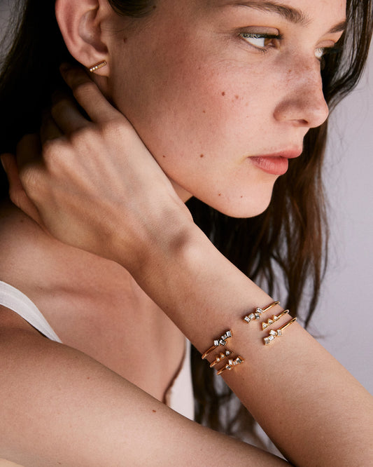 Close-up of a woman's arm with gold bracelets and earrings against a neutral background