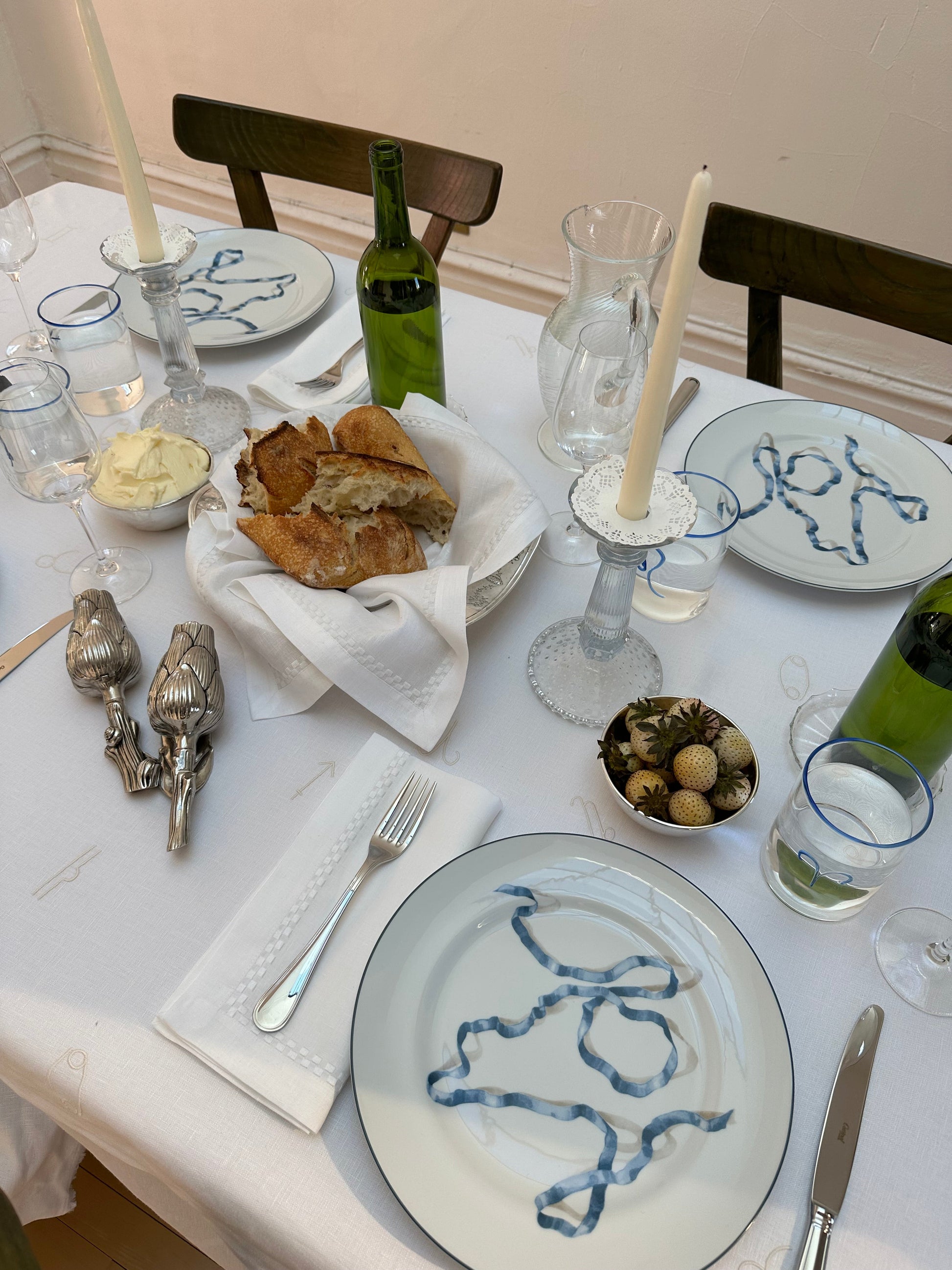 Dining table set with plates, bread, wine bottles, and glasses.