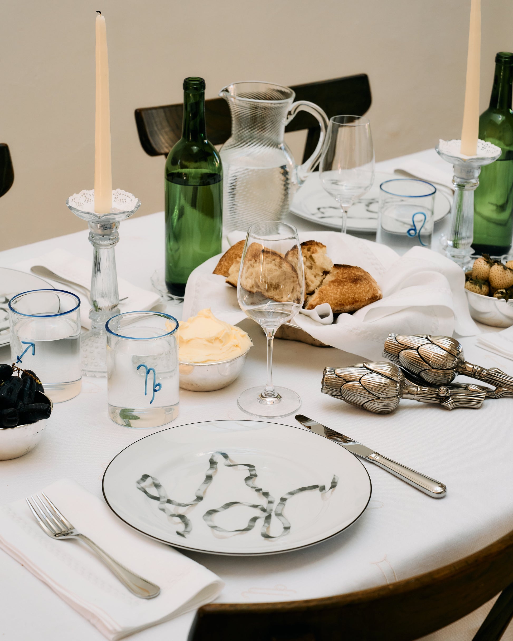 Dining table setting with plates, glasses, and bread on a white tablecloth.