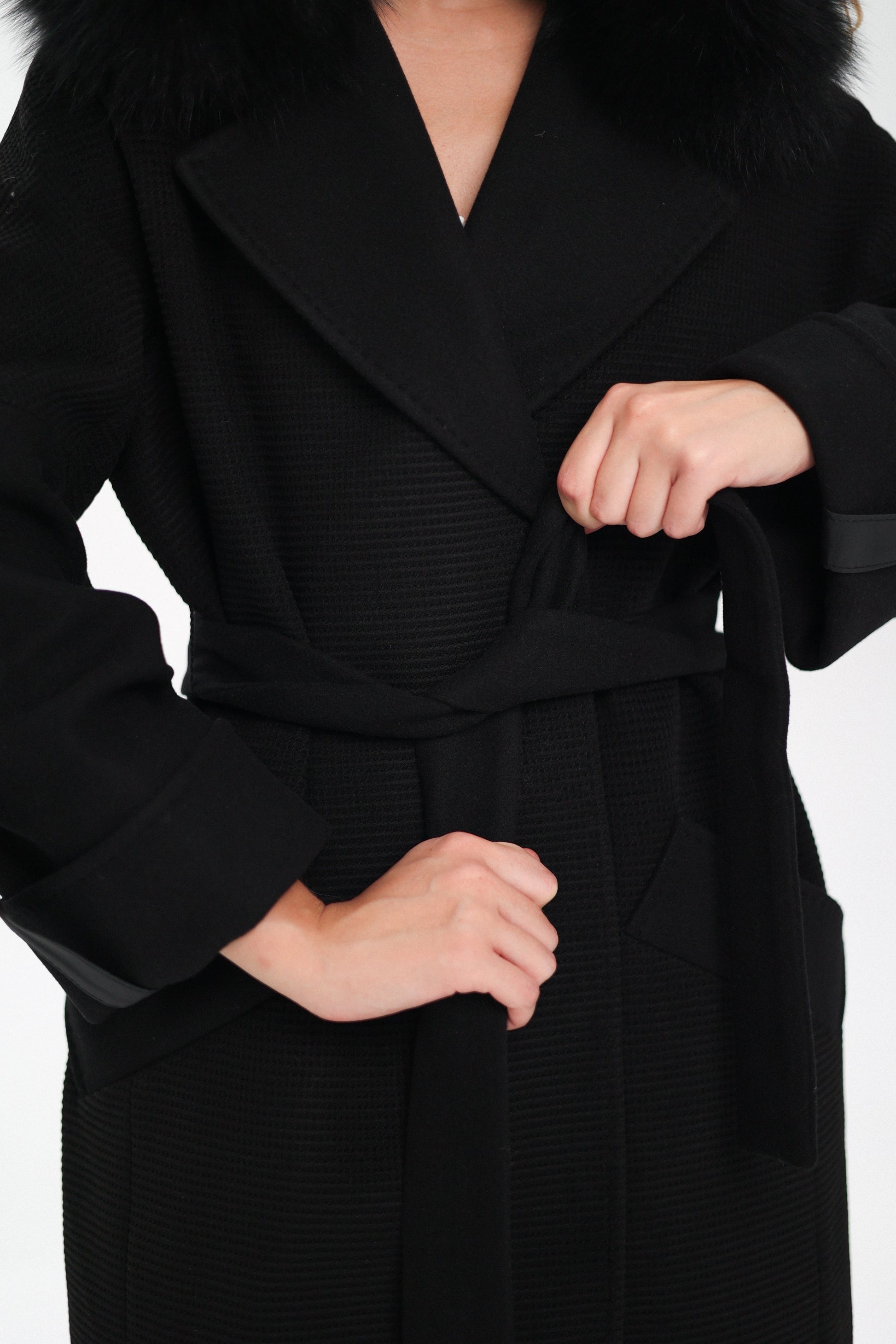 Black coat with a belt being adjusted on a white background