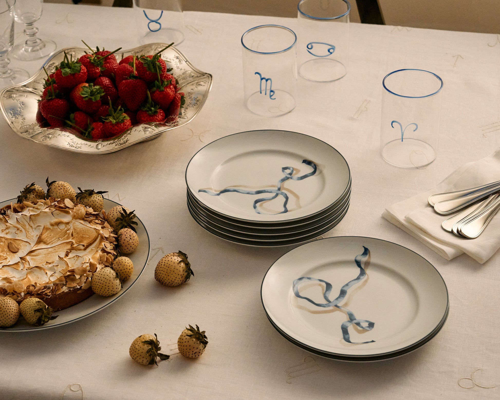 Table setting with plates, strawberries, and a cake on a white tablecloth.