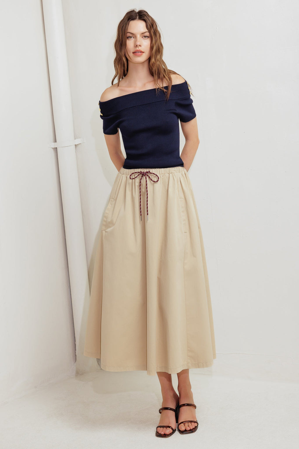 Woman wearing a navy off-shoulder top and beige skirt on a white background