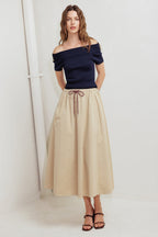 Woman wearing a navy off-shoulder top and beige skirt on a white background