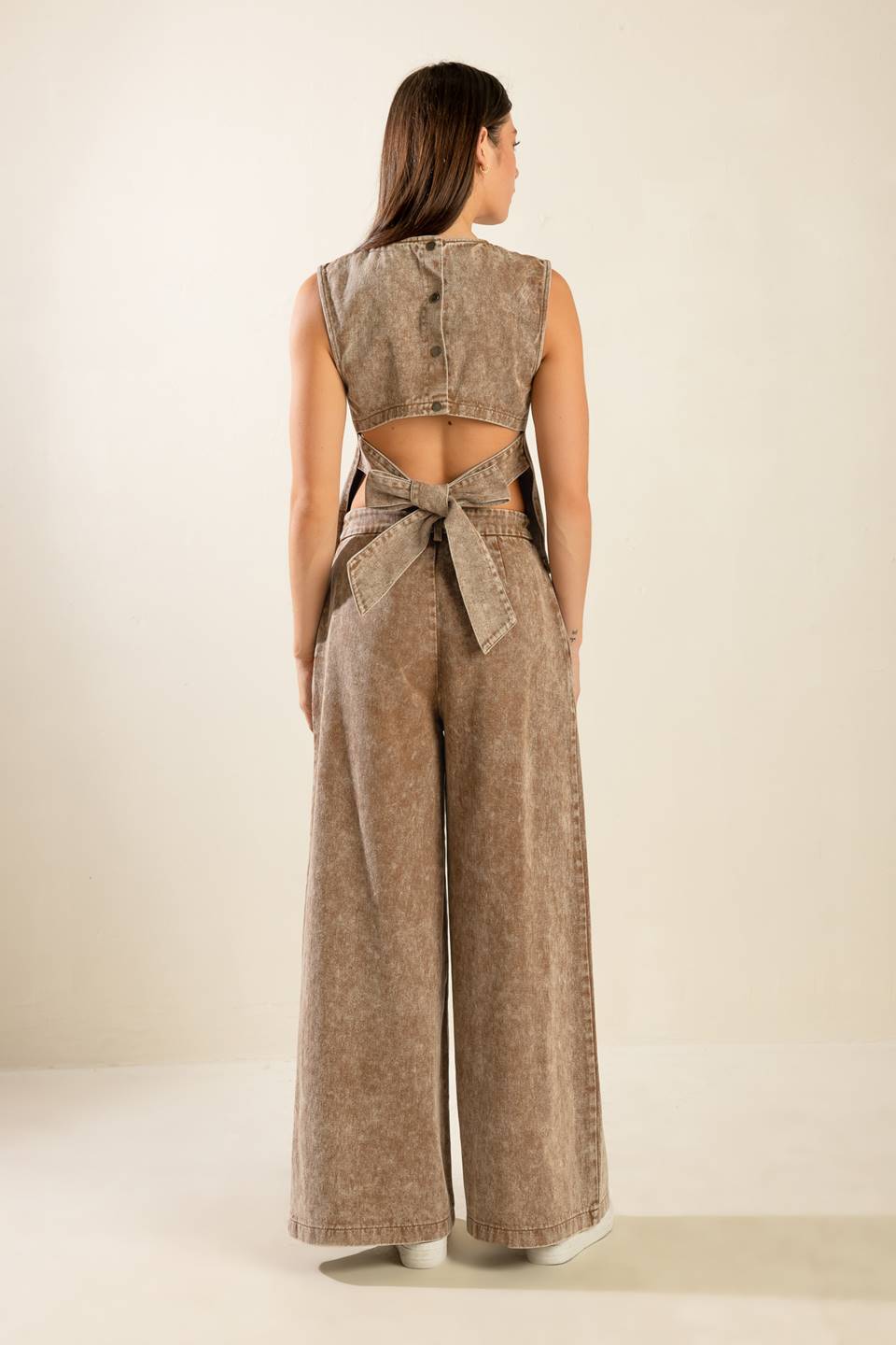 Woman wearing a beige sleeveless top and wide-leg pants with a belt on a plain background