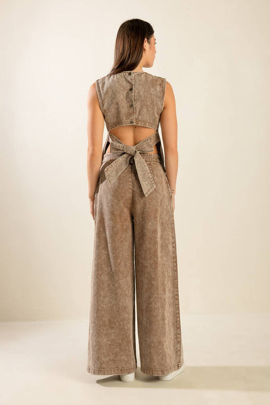 Woman wearing a beige sleeveless top and wide-leg pants with a belt on a plain background