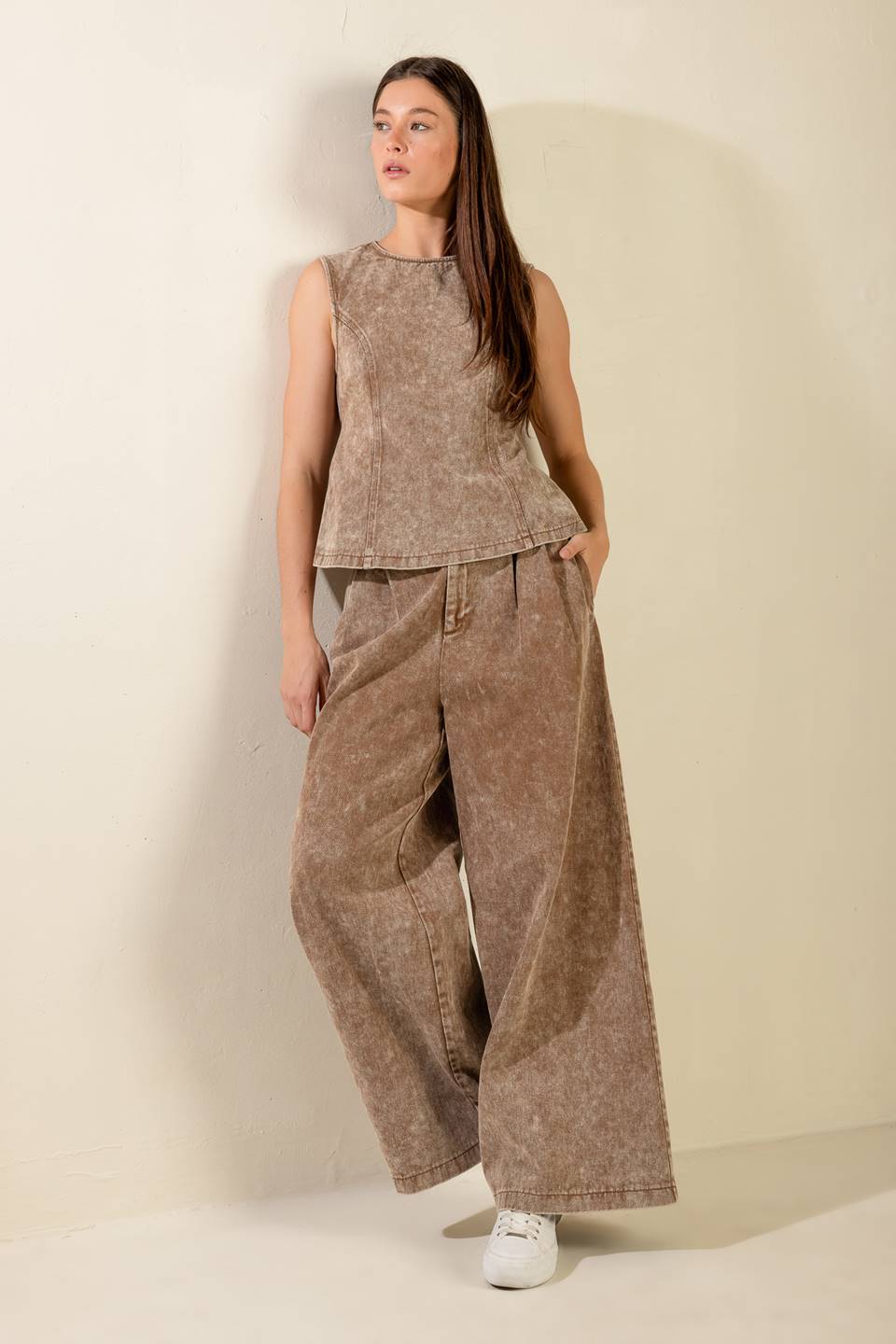 Woman wearing a brown sleeveless top and wide-leg pants against a beige background