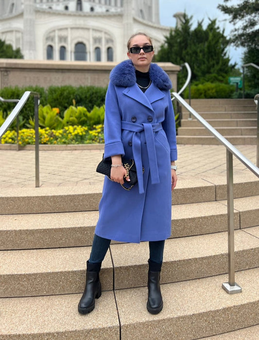 Person wearing a blue coat with fur collar standing on steps outdoors.