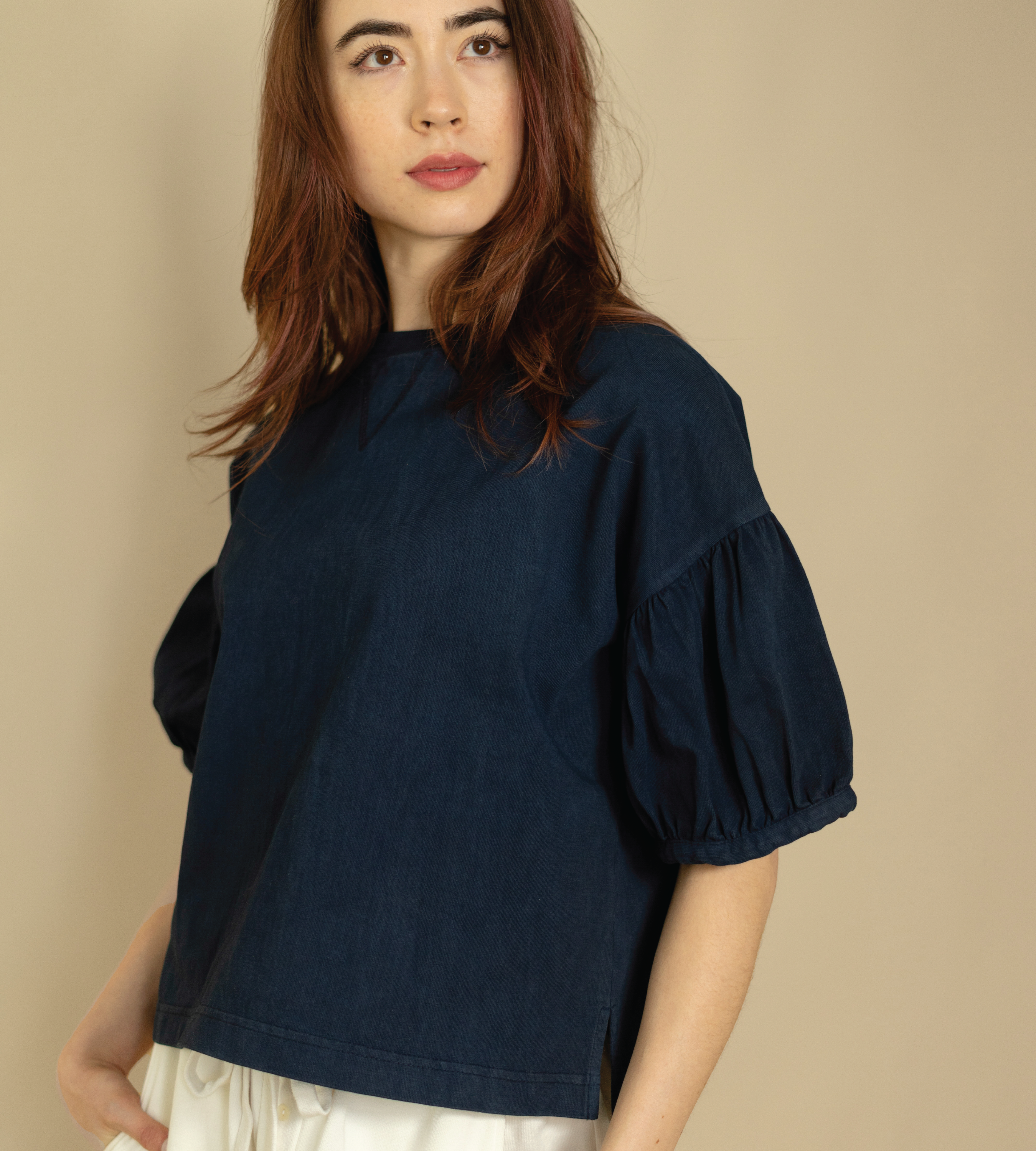 Woman wearing a navy blue blouse with puff sleeves against a beige background