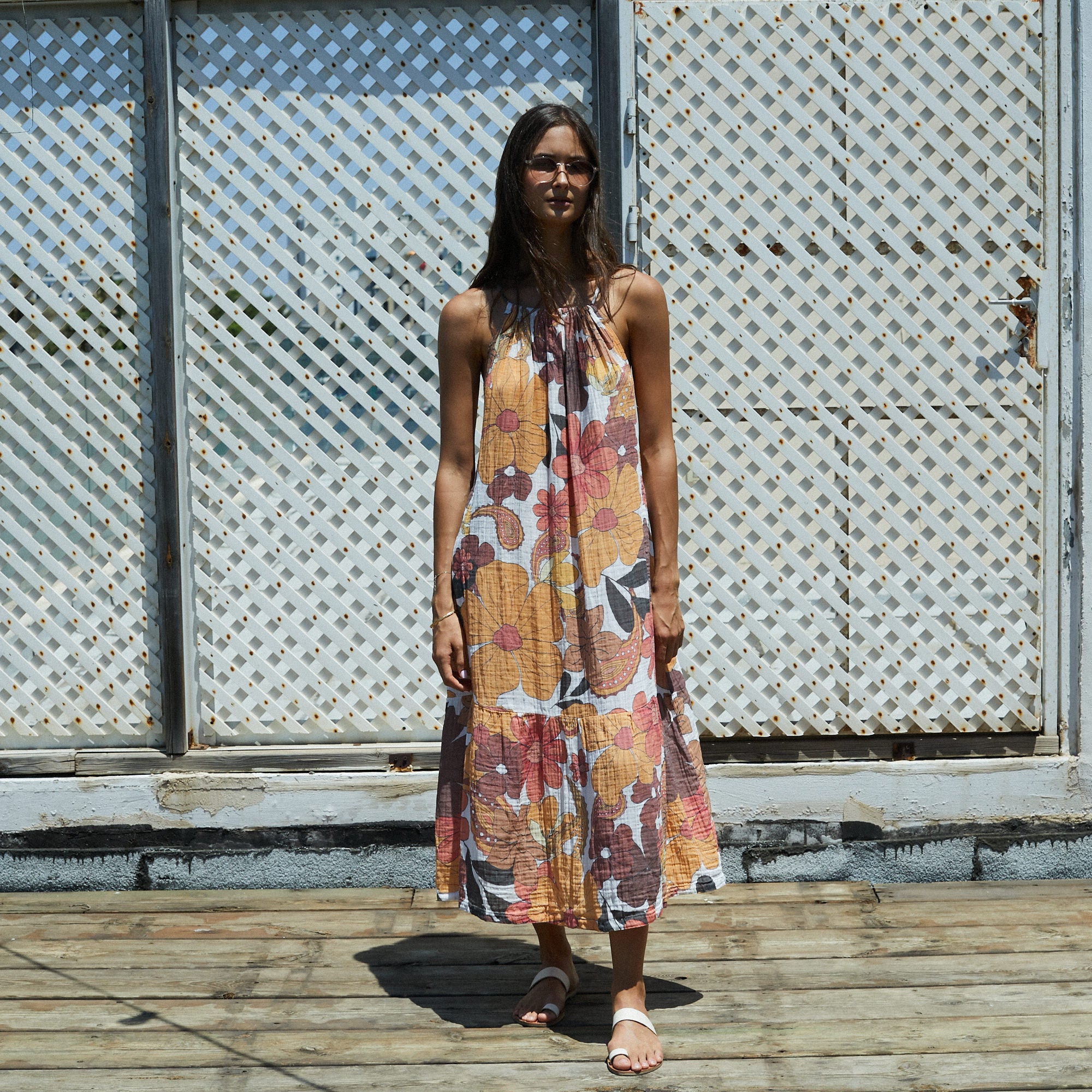 Woman wearing a floral dress standing on a wooden deck with a lattice background