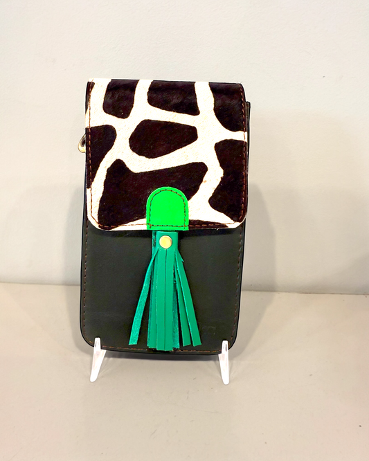 Small handbag with a cow print top section and green tassel on a stand against a light background