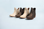 Pair of brown and beige ankle boots with studded details on a light blue background
