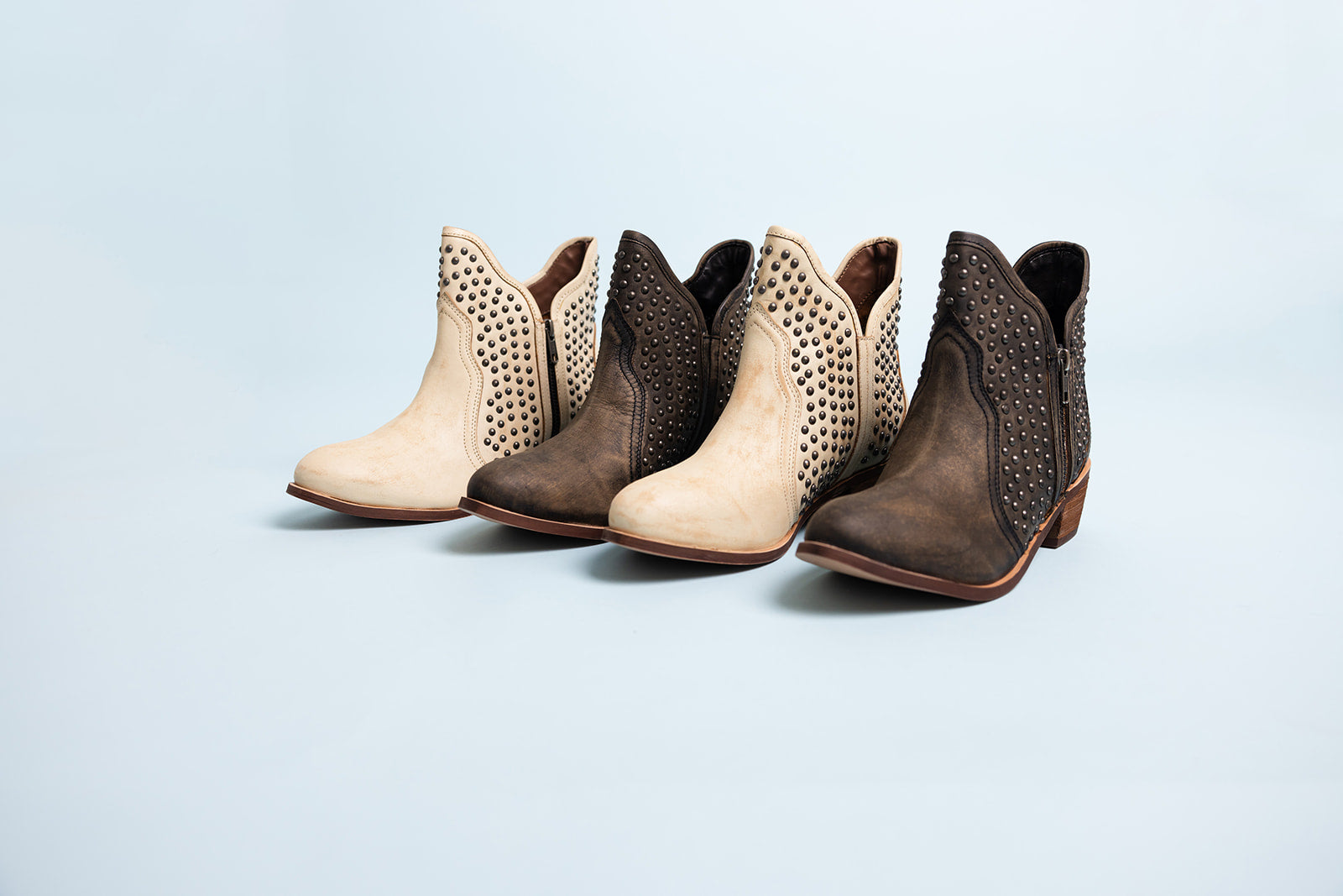 Pair of brown and beige ankle boots with studded details on a light blue background