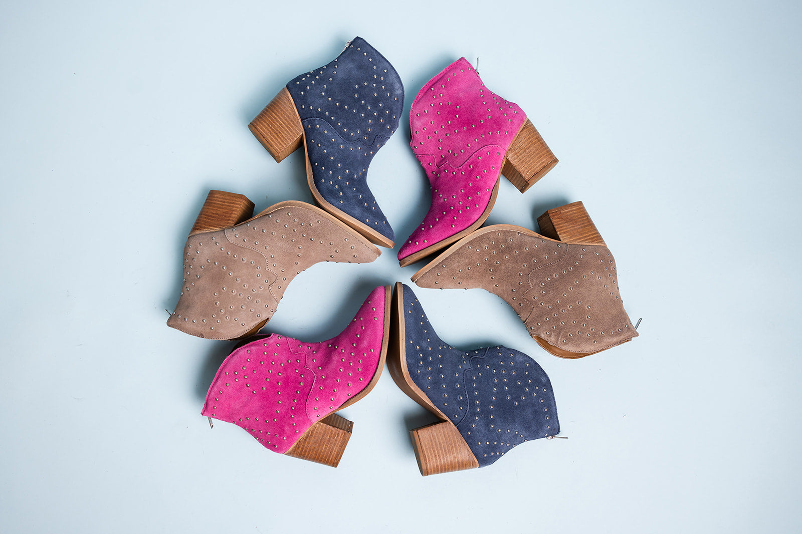 Five pairs of women's boots in pink, blue, and brown arranged in a circle on a light blue background.