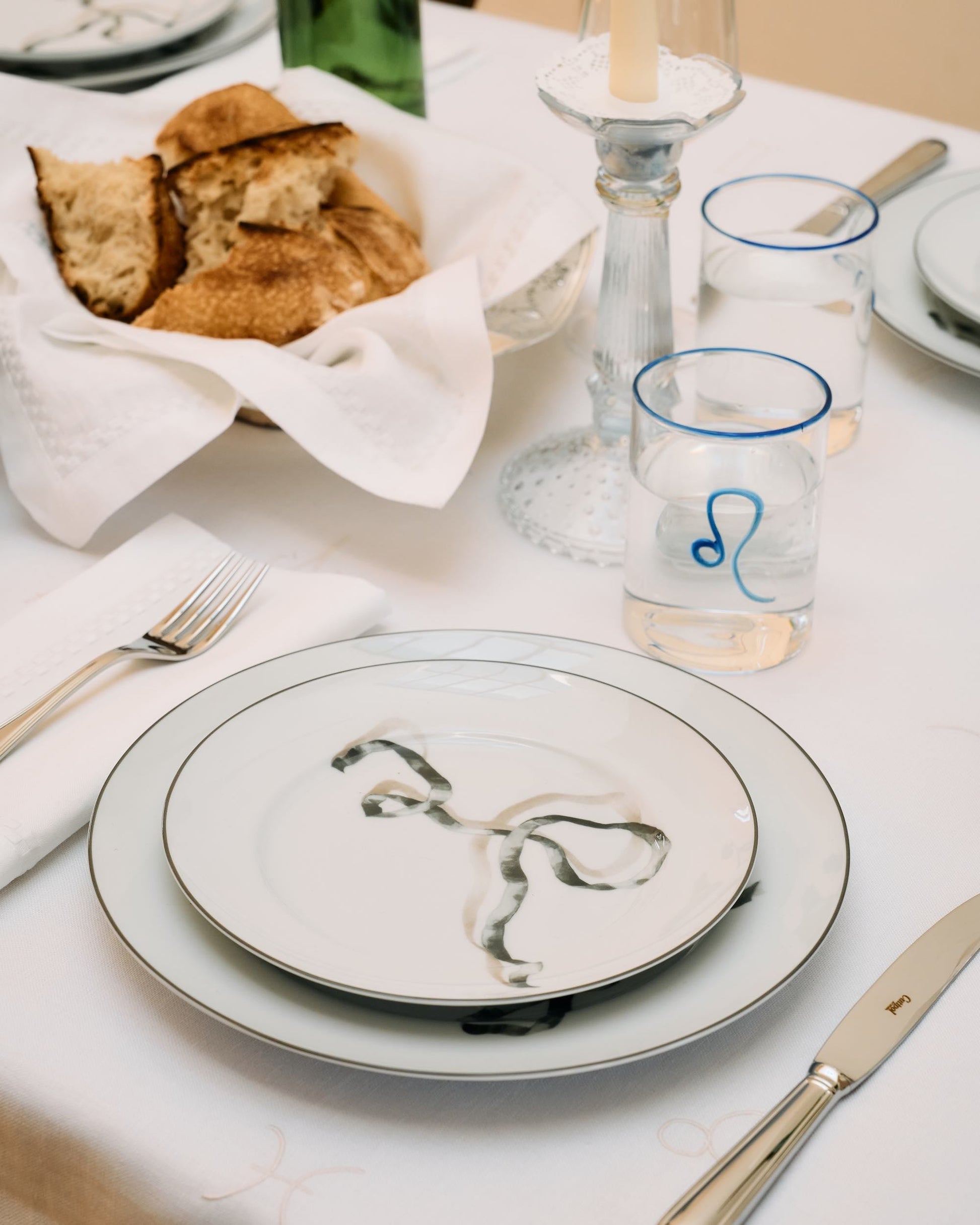 Dining table setting with plates, glasses, and bread on a white tablecloth.