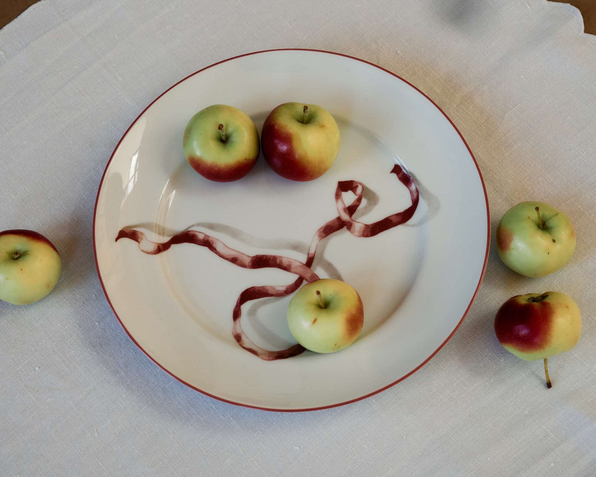 Apples arranged on a plate with a decorative branch on a white tablecloth.