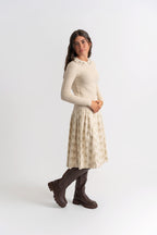 Woman wearing a beige sweater and patterned skirt with brown boots on a white background