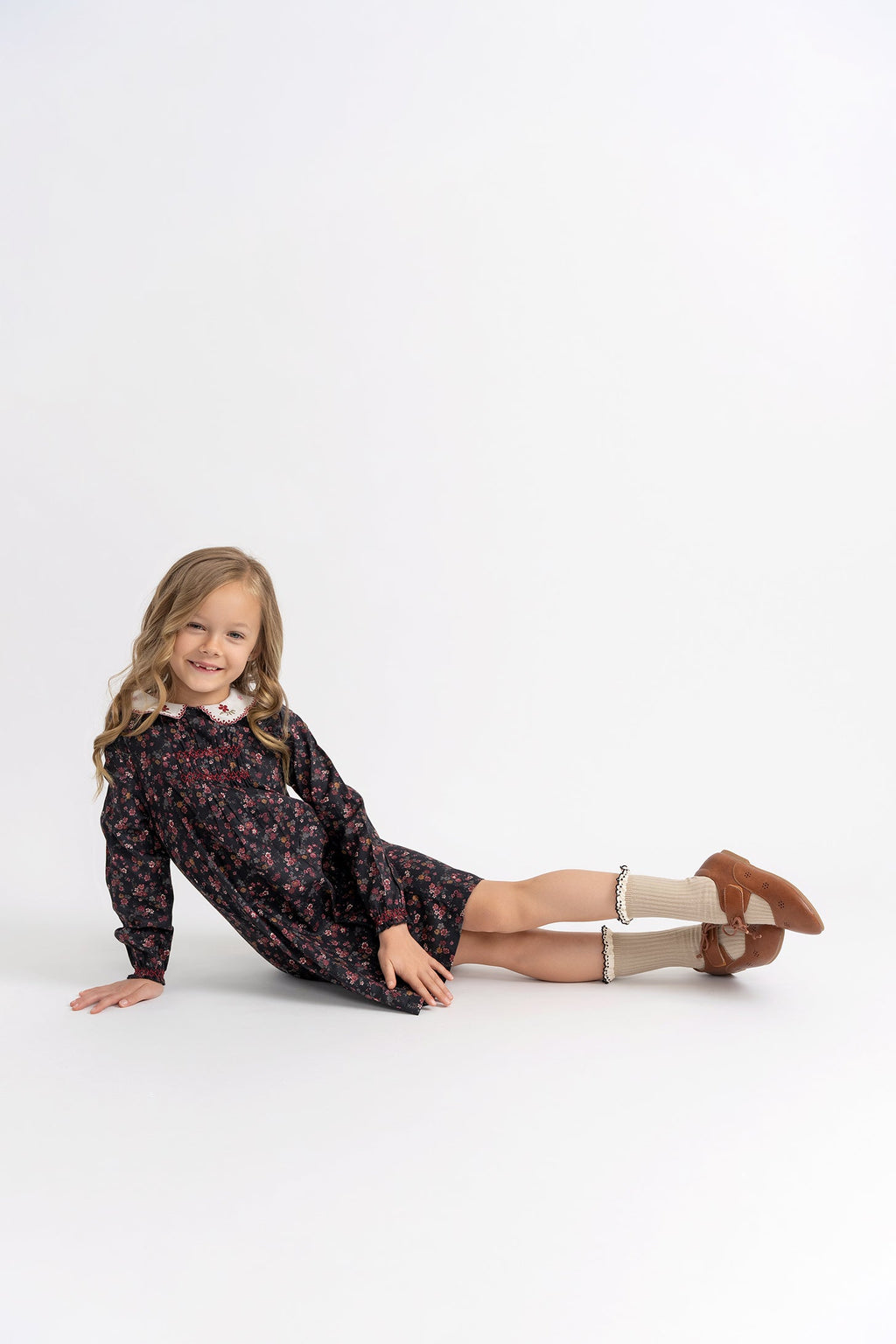 Young girl in a floral dress sitting on a white background