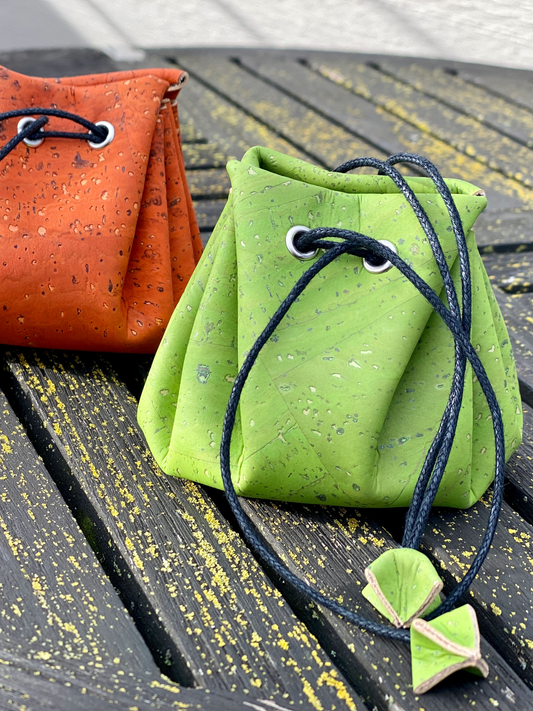 Green drawstring bag with leaf decorations on a wooden surface, next to an orange bag.
