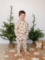 Child wearing gingerbread-themed pajamas standing in front of Christmas trees and gift boxes.