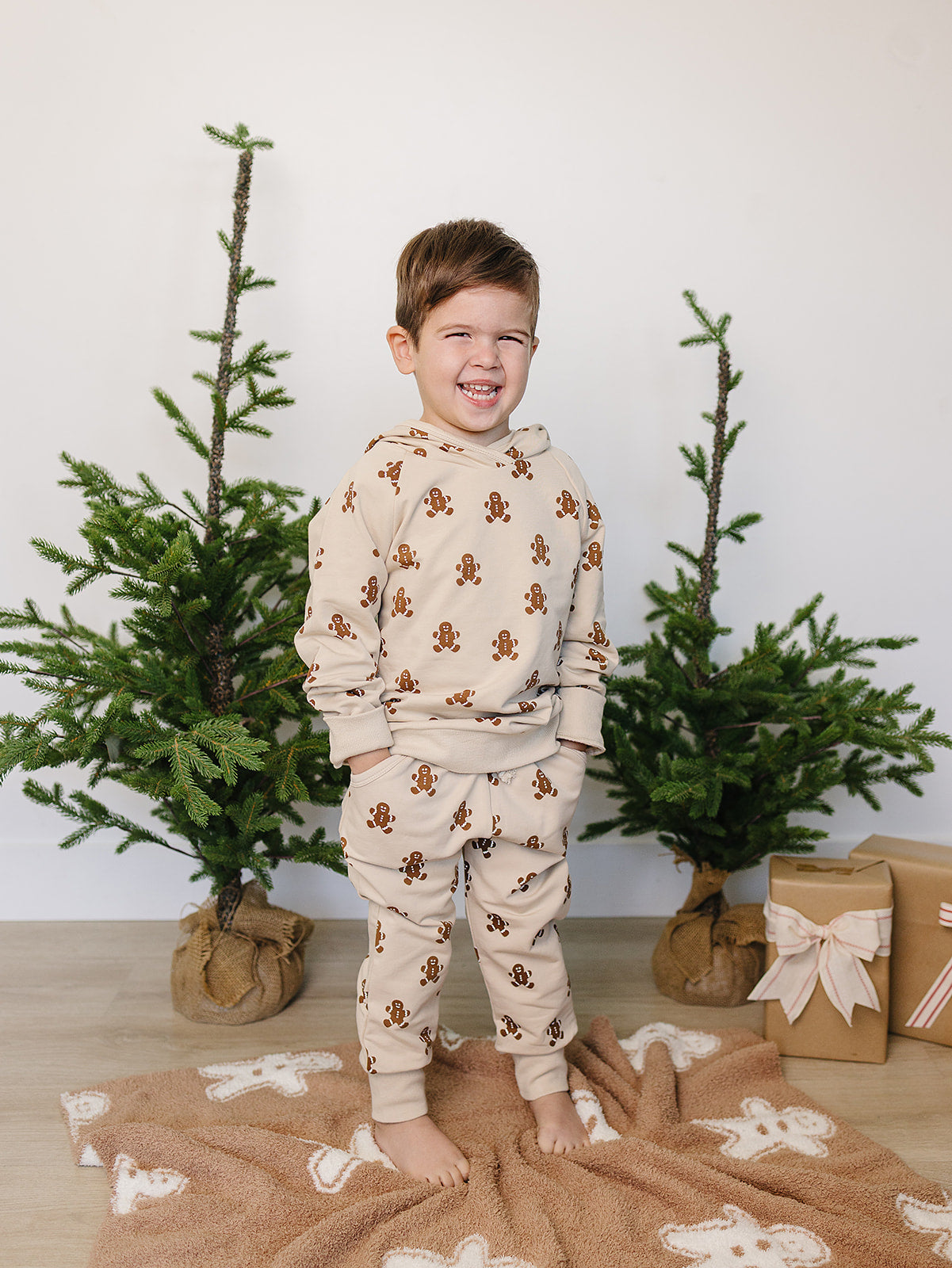 Child wearing gingerbread-themed pajamas standing in front of Christmas trees and gift boxes.