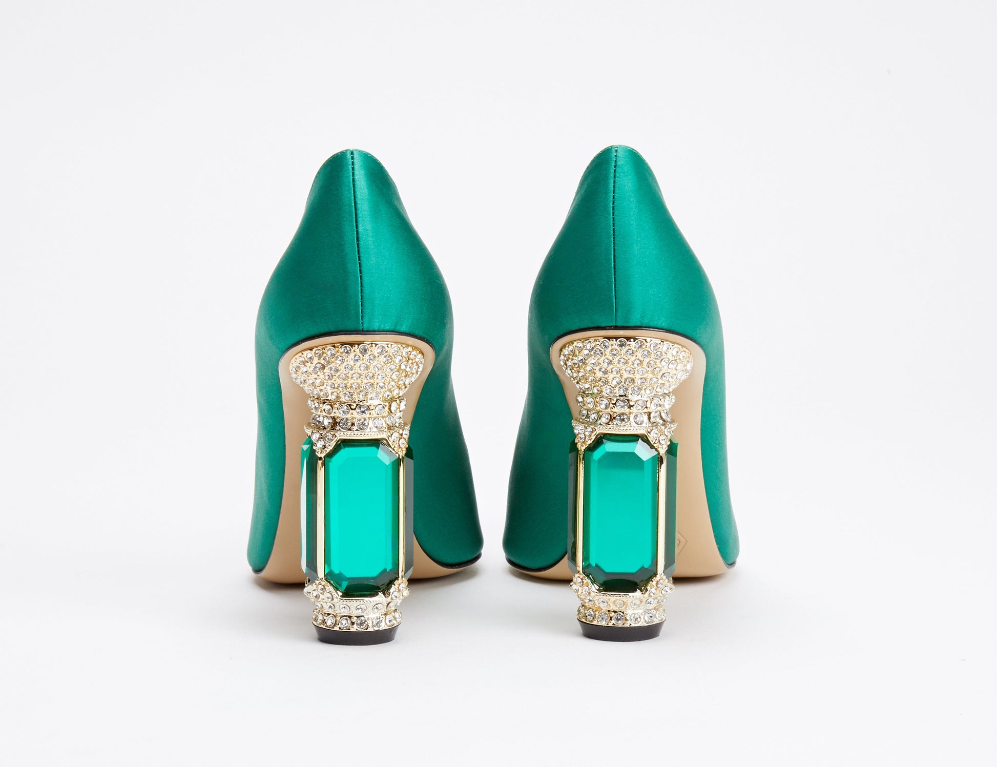 Pair of green high-heeled shoes with gold embellishments on a white background