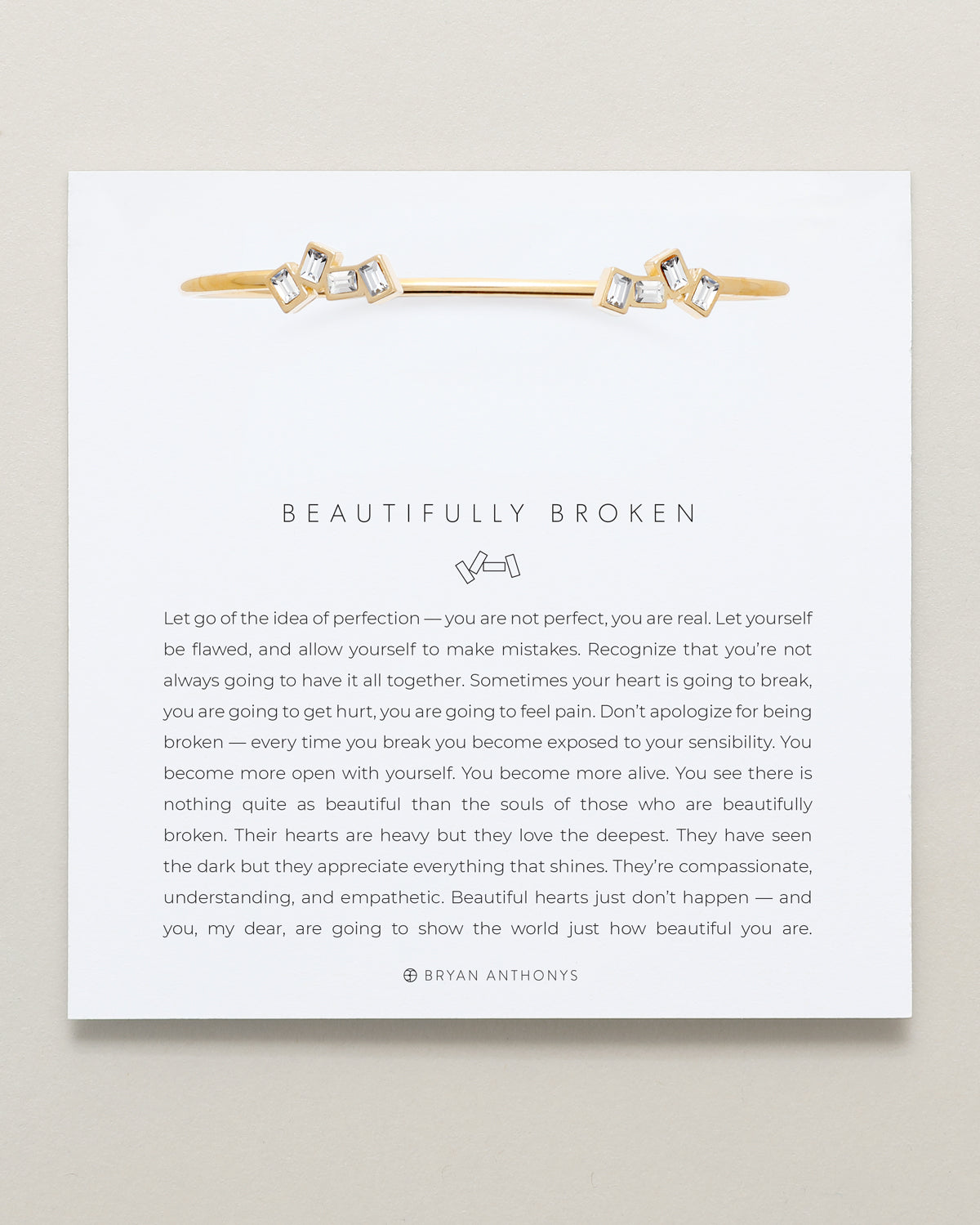 Gold and diamond bracelet on a white card with text and brand name.