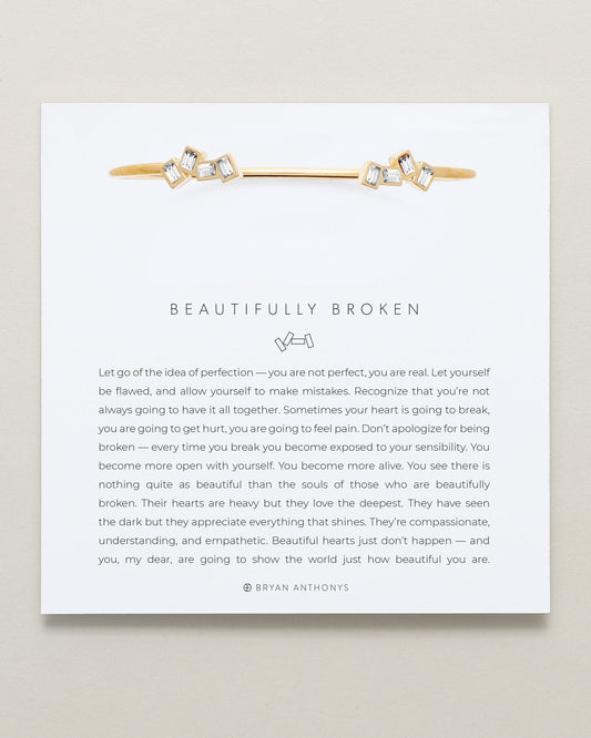 Gold and diamond bracelet on a white card with text and brand name.