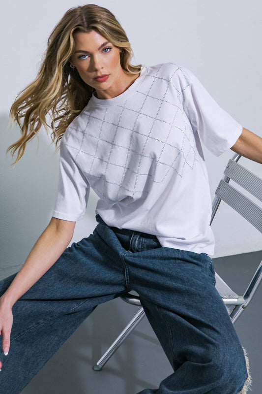 Woman wearing a white oversized shirt and blue jeans sitting on a chair against a gray background
