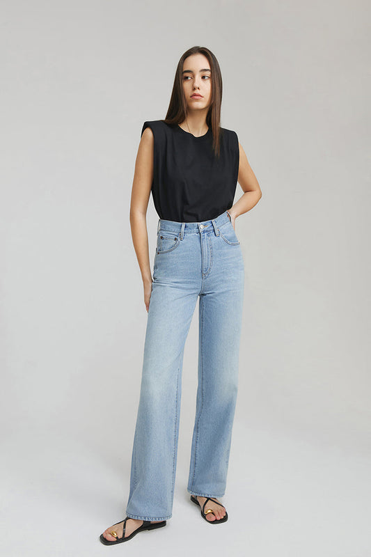 Woman wearing a black sleeveless top and light blue jeans on a plain background