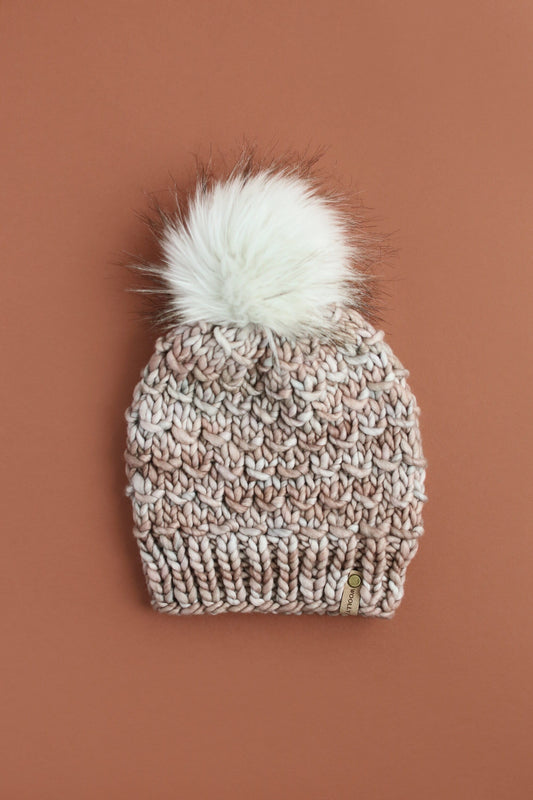 Knitted beanie with a fluffy pom-pom on a brown background