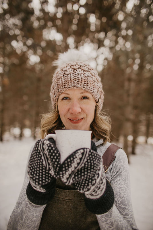 Woman in winter clothing holding a mug outdoors with blurred trees in the background