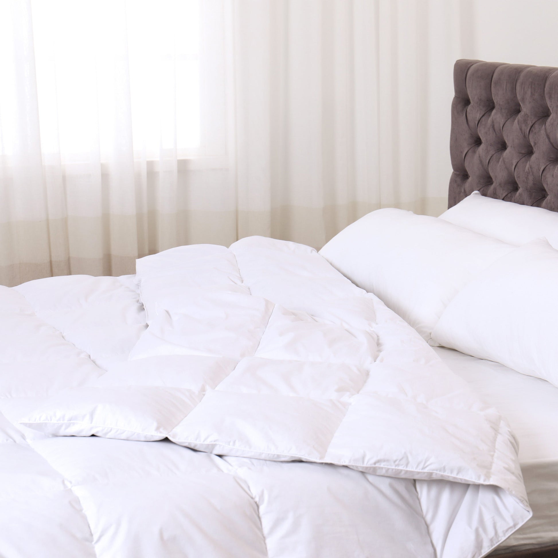 White comforter and pillows on a bed with a gray headboard.
