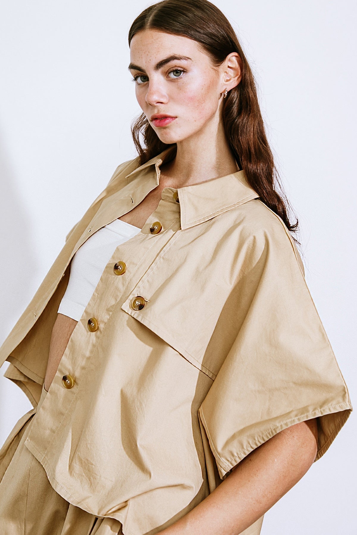 Woman wearing a beige jacket with gold buttons on a white background